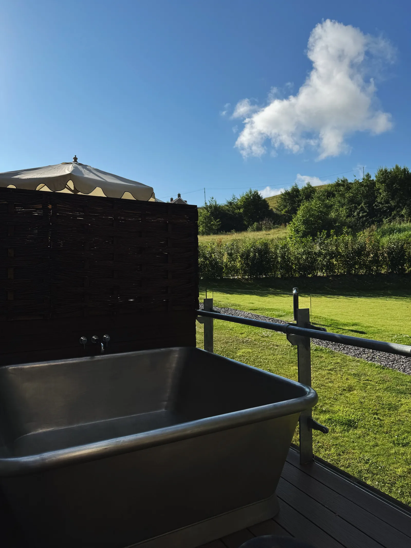 A large metal square tub on a secluded hotel deck overlooking a green hill