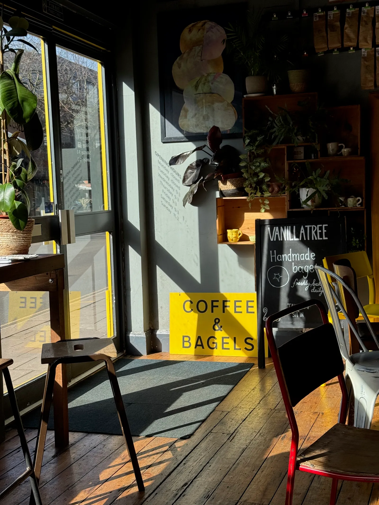 An interior shot of a cozy coffee shop with a bright yellow sign next to the entry way that says coffee