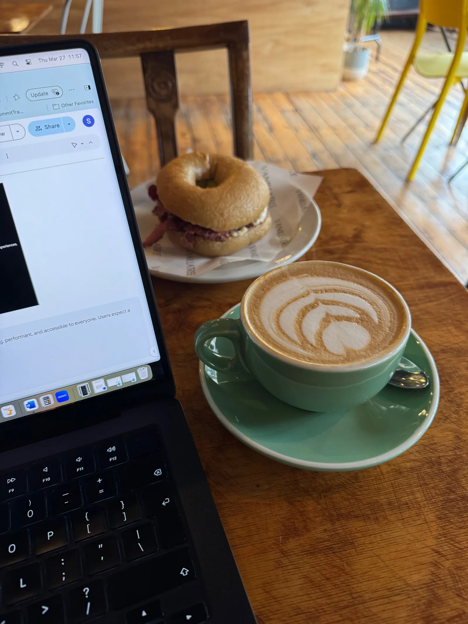 A cup of coffee and a bagel sandwich next to a laptop